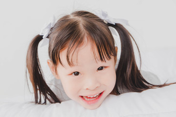 Fototapeta premium A little cute girl lying down on the bed looking and smiling in the white bedroom.
