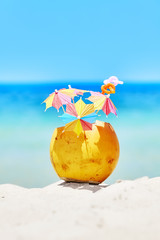 Coconut with colorful umbrellas and straws on a beach, summer fun holiday concept, selective focus.