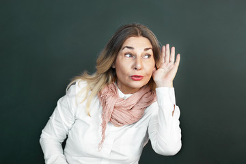 Nosy funny senior 60 year old woman holding hand to ear, trying to listen to juicy gossip or secret...