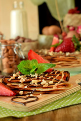 Fototapeta na wymiar Crepes decorated with nuts, chocolate, fresh strawberries and mint served on a wooden board