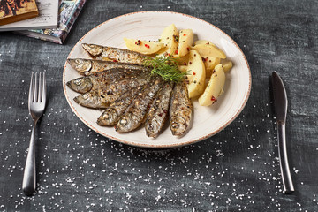 Fried sardines with boiled potatoes on a plate close up. horizontal