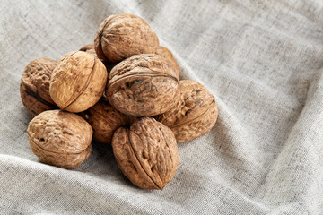 A stack of hard shells of walnuts piled together on light grey fabric cotton tablecloth, selective focus