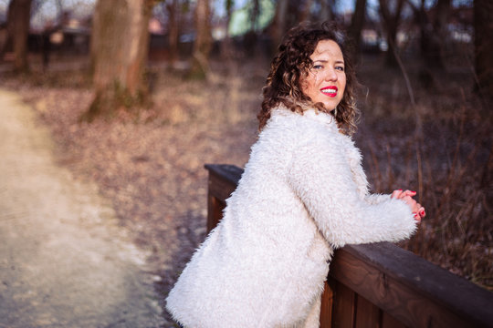Outdoor close up portrait of beautiful curly woman wearing fur coat at park