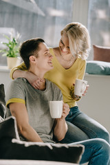 smiling couple holding cups of coffee and looking at each other at home