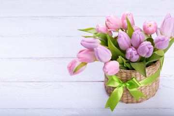Bouquet of pink tulips in a wicker basket on light gray background