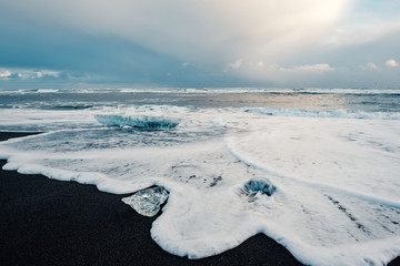 Ice on the black volcanic beach near Jokulsarlon glacier lagoon, winter Iceland. Detail of a glacial fragment of ice at black sand beach in beautiful evening light. © 1tomm
