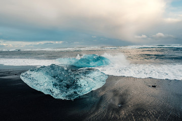 Ice on the black volcanic beach near Jokulsarlon glacier lagoon, winter Iceland. Detail of a glacial fragment of ice at black sand beach in beautiful evening light.