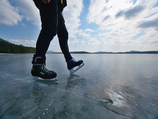 Man ice skating on frozen lake. Thin ice with deeep cracks below man - obrazy, fototapety, plakaty
