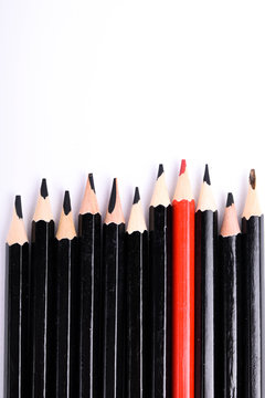 Red pencil standing out from crowd of plenty identical black fellows on white table. Leadership, uniqueness, independence,  initiative, strategy, dissent, think different, business success concept