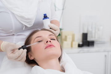 partial view of young woman receiving facial treatment made by cosmetologist in salon