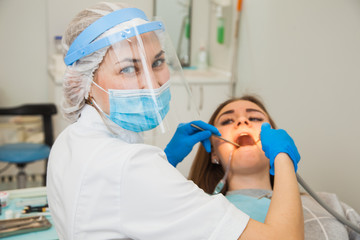 Female stomatologist in blue protective mask examining patient's teeth. Dentist caries treatment at dental clinic office. People, medicine, stomatology and health care concept