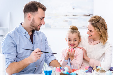 Obraz na płótnie Canvas Child holding Easter egg by smiling parents
