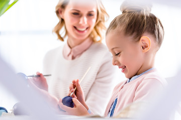 Young woman and child girl painting Easter eggs