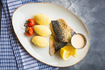 Dish with grilled fish, millet porridge, tomato, lemon slice and shrimp sauce
