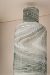 Gray with a divorce vase decorative in the form of a bottle. On a white shelf.