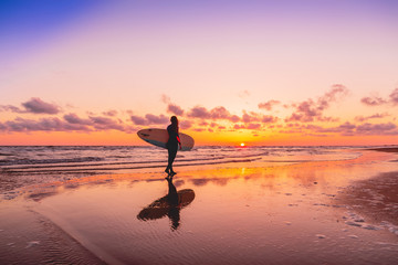 Silhouette and reflection of surfer girl with surfboard on a beach at sunset. Surfer and ocean