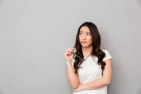 Pensive asian woman in t-shirt holding eyeglasses and looking away