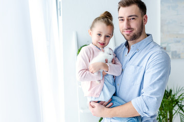 Smiling father embracing daughter with rabbit in hands