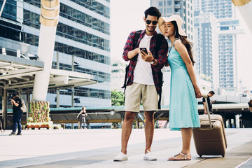 Fototapeta premium Couple Asian travelers are walking on city street and looking at interesting places to travel from smart phone. Vacation and technology Concept