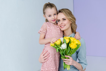 Fototapeta na wymiar Woman holding bouquet and embracing cute daughter on women's day