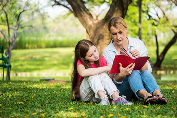 Mother and daughter reading a book together in a park. Family, lifestyle and education concept