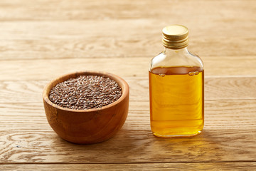 Composition of glass oil jars, wooden bowl and scoop with flax seeds, selective focus