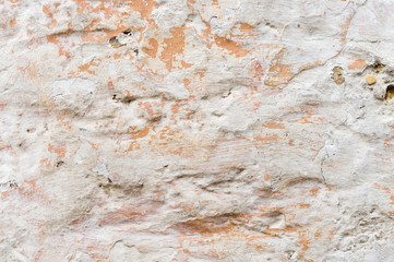 Textured grunge background. Volumetric plastered wall with a multilayer cracked coating. Orange chips on the whitewashed wall. Grunge texture with a deep pattern