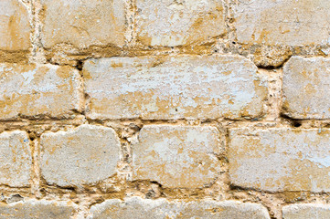 Textured background of a multi-colored brick painted in yellow. A sizzling yellow paint on an old broken brick. Grunge style