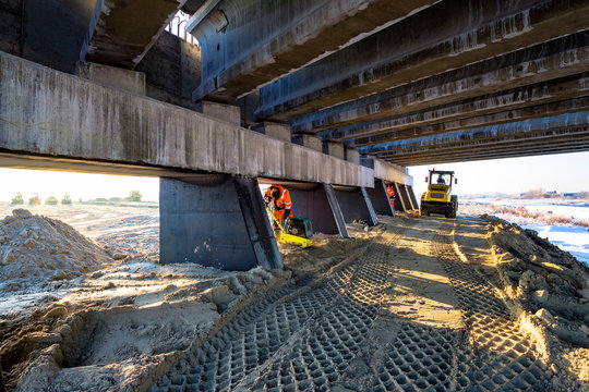 Construction Of An Overpass. Roller Compacts The Soil In Embankment On The Road's Construction. Sand Consolidation On Road-building. Wheel Marks On The Sand. Bridge Support. Hard Work Road Worker