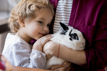 Close up portrait of cute blond toddler hugging pet bunny and clinging to mom