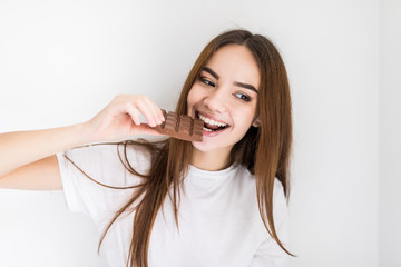 Woman eating chocolate. Beautiful young woman eating chocolate on white wall
