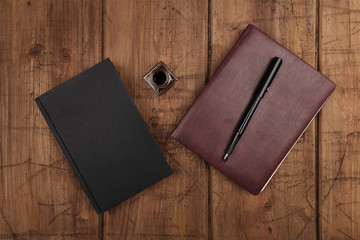 A black book, a leather journal, and ink well and pen