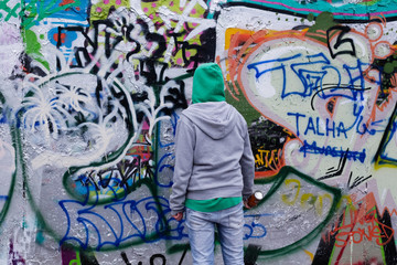 A person holding a can of spray facing a wall full of graffiti