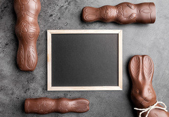 Chocolate Easter bunnies and empty blackboard on rustic background