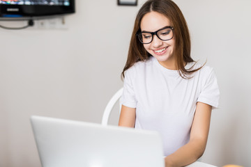 Beautiful young woman with coffee using typing laptop in the kitchen in the morning