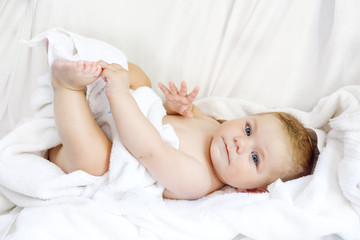 Obraz na płótnie Canvas Cute little baby playing with own feet after taking bath. Adorable beautiful girl wrapped in white towels