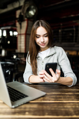 Woman typing write message on smart phone in a modern cafe. Cropped image of young pretty girl sitting at a table with coffee or cappuccino using mobile phone.