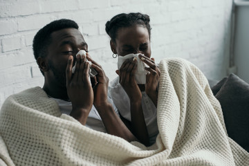 young african american couple holding paper napkins while having flu together at home