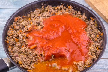 Preparation of bolognese sauce - adding tomato paste to fried minced meat in a frying pan
