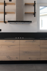 New crafted kitchen in wood, stainless steel and black granite just set up in a new apartment. Interior industrial design with exposed shelves and dark gray floor. Oak wood, black color and inox steel