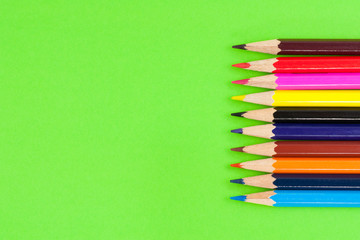 Row of colorful wooden pencils on background of green paper. Top view
