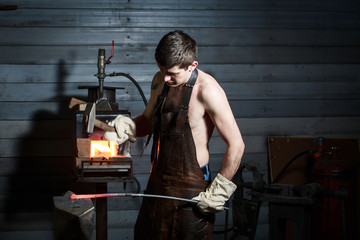 Young muscular man working on a blacksmith with metal