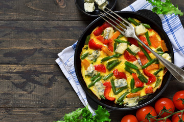 Omelette with vegetables and blue cheese for breakfast on a wooden background.