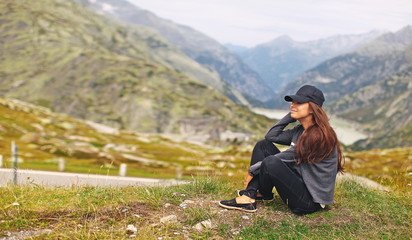 young woman tourist on a background of mountainous natural scenery sits on the edge of the cliff