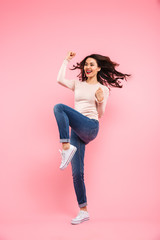 Full length photo of joyous woman with long brown hair expressing happiness and luck with clenching fists, isolated over pink background