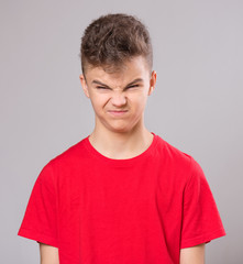 Teen boy making silly grimace - expressing disgust face. Upset child on gray background. Emotional...