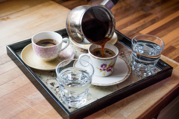 Pouring Turkish Coffee served with water in tray.