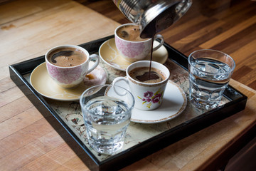 Pouring Turkish Coffee served with water in tray.