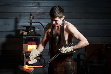 Young muscular man working on a blacksmith with metal
