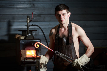 Young muscular man working on a blacksmith with metal